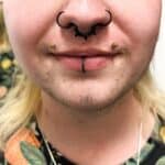 Close-up of a person’s lower face with septum, vertical labret, and dimple piercings, wearing a patterned shirt with fruit designs.