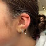 A close-up of a person's ear with a bun hairstyle, showing multiple gold hoop earrings and one small diamond stud.