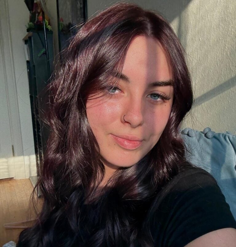 A woman with long, wavy dark hair and a nose ring poses for a selfie indoors, sunlight and shadows highlighting her face—capturing the confidence often seen in top sales associates.